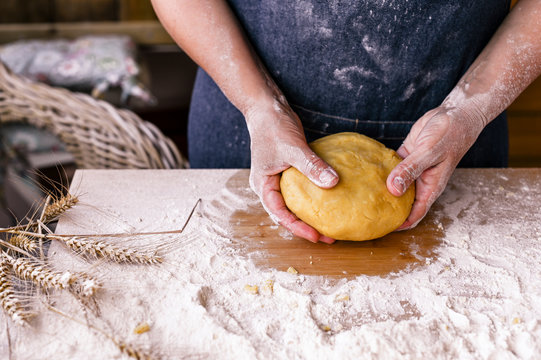 Female hands and dough. A woman is preparing a dough for home baking. Rustic style photo. Wooden table and flour. Free space for text.