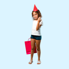 Full body of Little girl at a birthday party holding a gift bag presenting and inviting to come on blue background