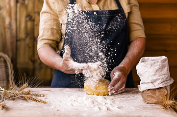 Women's hands, flour and dough. Levitation in a frame of dough and flour. A woman in an apron is preparing dough for home baking. Rustic style photo. Wooden table, wheat ears and flou.Emotional photo