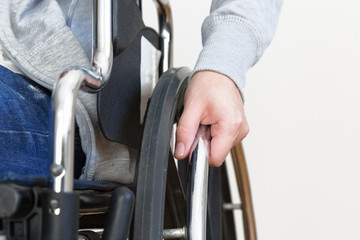Detail of disabled woman holding a hand on wheel of a wheelchair.