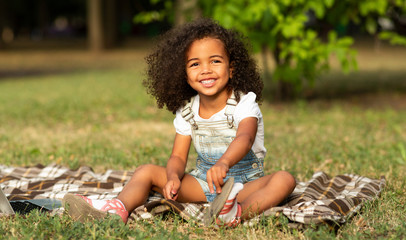 Adorable girl sitting on blanket at nature, enjoying summertime