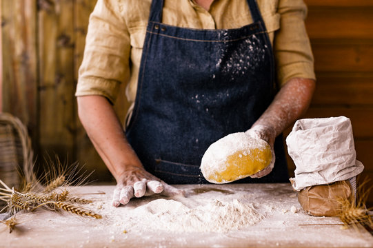 Female hands and dough. A woman is preparing a dough for home baking. Rustic style photo. Wooden table, wheat ears and flour. Free space for text