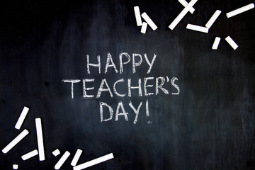 Back to school, college, university concept. Congratulatory inscription of happy teachers day on blackboard background from pupils. Pieces of white chalk are scattered on black canvas.