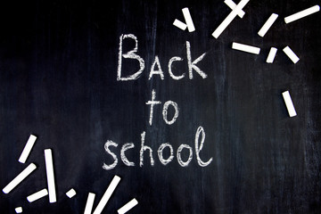Inscription of back to school on classroom blackboard background. Pieces of white chalk are scattered on black canvas. Preparing pupils students for study at college, university, academy.