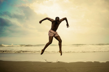 dramatic contemporary dance choreographer doing ballet beach workout . young attractive and athletic afro black American man dancing on sunrise jumping