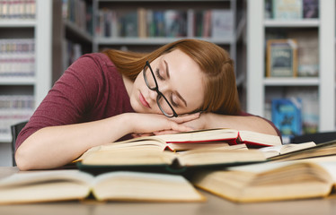 Tired girl with glasses having nap on books in library