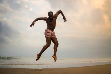 Fototapeta na wymiar dramatic contemporary dance choreographer doing ballet beach workout . young attractive and athletic afro black American man dancing on sunrise jumping