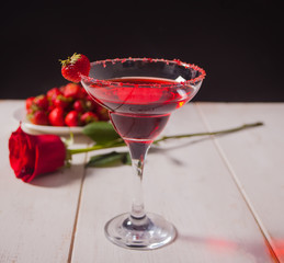 Red exotic alcoholic cocktail in clear glass, plate with berries and red rose for romantic dinner.