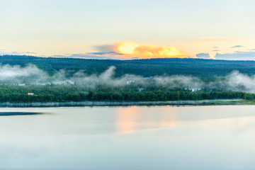 Misty vapor at a lake in a forest at dusk