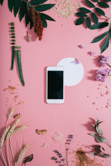 White phone with a clear screen and white circle shape in flowers on pink background. Flat lay. Top view