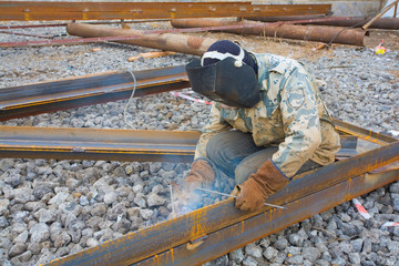 Welder in mask welding metal construction on open air.