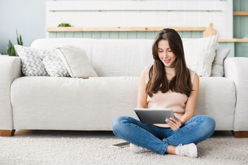 Beautiful  young woman with digital tablet relaxing at home. Happy smiling girl sitting in living room using tablet pc. Resting, relaxation, technology concept
