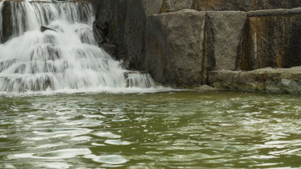 Fototapeta na wymiar Small waterfall flows into a pond. rushing stream water