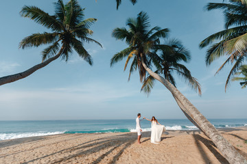 Bride and groom standing under palm tree on a tropical beach. Wedding on the beach and first dance...