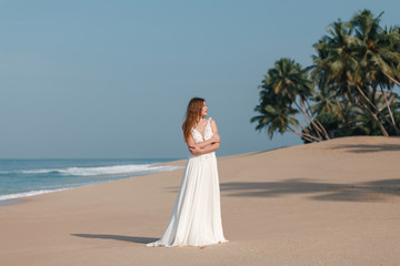 Fototapeta na wymiar Beautiful young woman in white wedding enjoying a day at the beach. A beautiful bride in a white wedding dress is walking along the beach, wedding concept