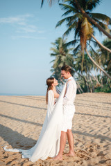 Happy just married couple on tropical white sand beach smiling and looking at each other during their wedding photoshoot in tropical country. Honeymoon in Sri Lanka