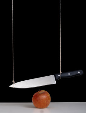 Sword of Damocles threat, risk concept, metaphor - large knife tied and suspended over apple. Still life with black background.