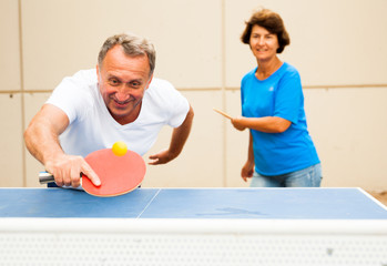 Happy mature man and woman playing table tennis