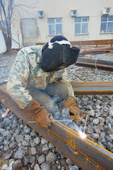 Welder in mask welding metal construction on open air.