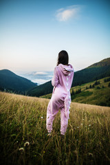 Slim lady in pink Dragon Pajamas in the mountains. Women in pink night-suit. Animal Cosplay Costume. Summer adventure journey in mountain nature outdoors