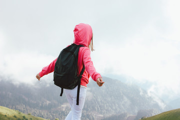 Tween girl with backpack looking on beautiful mountains in clouds, family travel concept