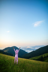 Positive young woman hiker in pink Dragon Pajamas open arms at mountain peak. Slim lady in pink night-suit. Funny travel, Animal Cosplay Costume. Summer adventure journey in mountain nature outdoors - 284524289