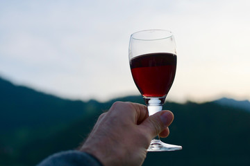 man hand holding a glass of red wine in front of blurred sunset horizon