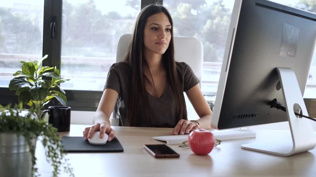 Smiling young business woman using her mobile phone while working with computer in the office.