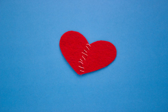 Red heart made of cloth with white thread on a blue background the Concept of Sadness, unrequited love, a broken heart.