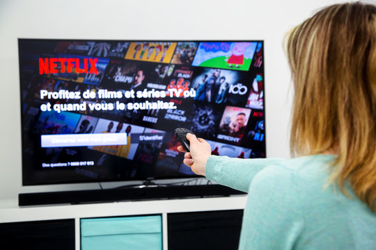 Woman Holding a TV remote control and switching channels on France Netflix HomePage