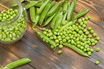 Fresh green peas in a glass jar and scattered peeled beans on dark wooden background. Top view. Rustic table.