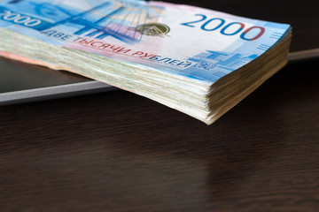 Payments for computer work concept. Stack of russian rubles lay on laptop keyboard. Wooden table with copy space.