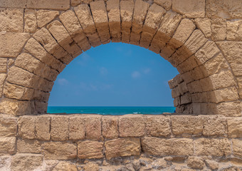 Ruins of the Roman aqueduct arches on the beach of Caesarea Israel with blue see and sky