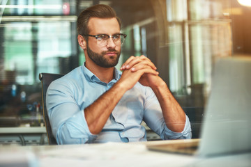 Smart and confident. Young bearded businessman in eyeglasses and formal wear looking at laptop...