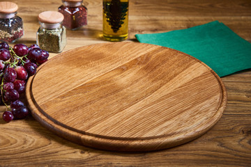 composition for preparing pizza with a wooden round board, jars of spices, olive oil bottle, grape on wooden background