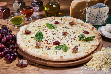 classic italian four cheese pizza served on a wooden round board. wooden table with ingredients, spices and sauces