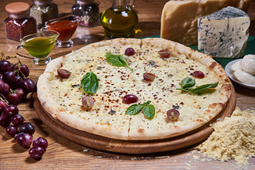 Four cheese pizza quattro formaggi with basil leaf on a rustic wooden board background