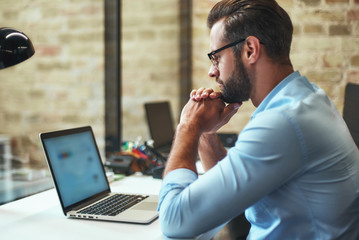 Concentrated on work. Side view of young bearded businessman in eyeglasses and formal wear looking...