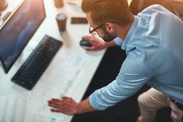 Work hard. Young bearded businessman in eyeglasses and formal wear using computer while standing in...