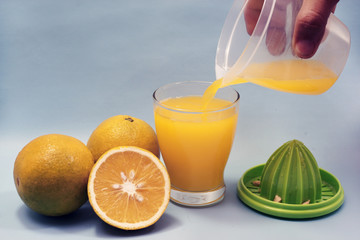 Fresh orange juice is poured from a jar into a glass and orange slices  isolated on blue