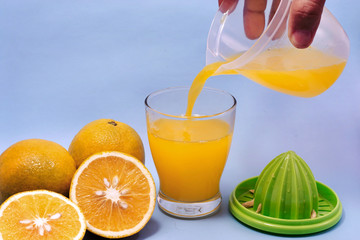 Fresh orange juice is poured from a jar into a glass and orange slices  isolated on blue