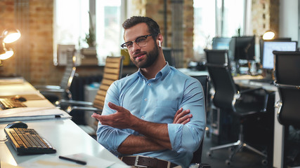Business talk. Portrait of young bearded man in eyeglasses and headphones talking with client while...