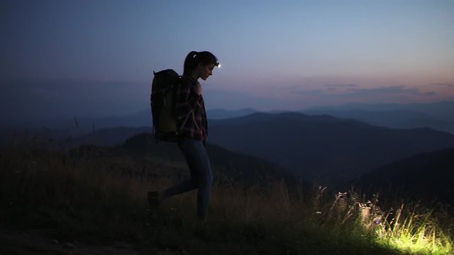 Happy woman traveler with headlamp flashlight hiking in the mountains. Summer adventure journey in mountain nature outdoors. A brilliant sunset over the mountains. High iso with Noise