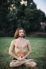 Yoga at park. Bearded man in lotus pose sitting on green grass. Concept of calm and meditation.