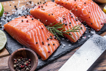 Fresh salmon fillets on black cutting board with herbs and spices.