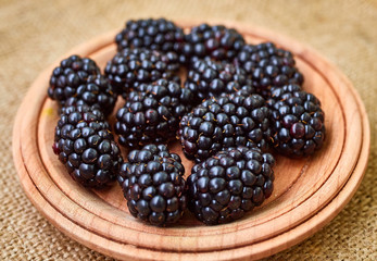 Fresh ripe blackberries in wooden plate on rustic table