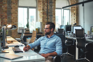 Businessman at work. Young andsuccessfulbearded man in eyeglasses and formal wear looking at...