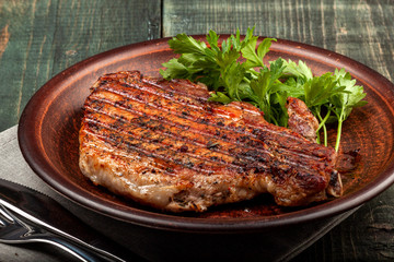a piece of fried pork with herbs on a white dish on a wooden table, closeup view
