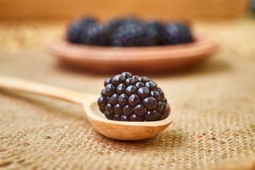 Closeup shot of fresh ripe blackberries in wooden spoon and plate on rustic table