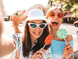 Two young smiling hipster women in casual summer clothes. Girls taking selfie self portrait photos...